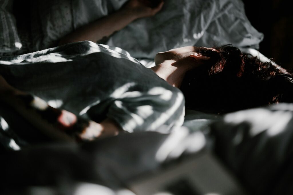 A person laying in a bed under a blanket.